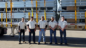 4 men in white shirts standing in front of 27 Delta TL-2+ crash cushions securely attached to a flatbed tractor trailer.