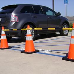 4' - 6.5' Black and Yellow Retractable Cone Bars (#15046A-CBYB) with 3x 28" Enviro-Cone construction cones cordoning off a handicap parking zone.