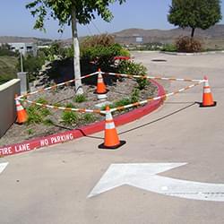 5.5' - 10.5' Orange and White Cone Bars (#150610A-CBOW) with 4x 28" Enviro-Cone construction cones cordoning off a section of parking lot landscaping.