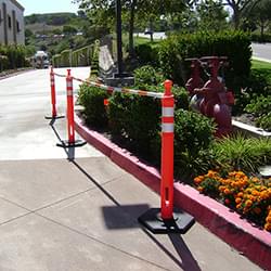 5.5' - 10.5' Orange and White Cone Bars (#150610A-CBOW) with 3x Grabber-Tube II's cordoning off a section of parking lot landscaping.