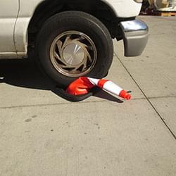 An Enviro-Cone construction cone being crushed underneath the tire of a moving vehicle